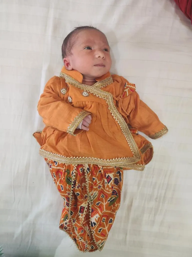 Baby in an orange printed kurta set lying on a white bed