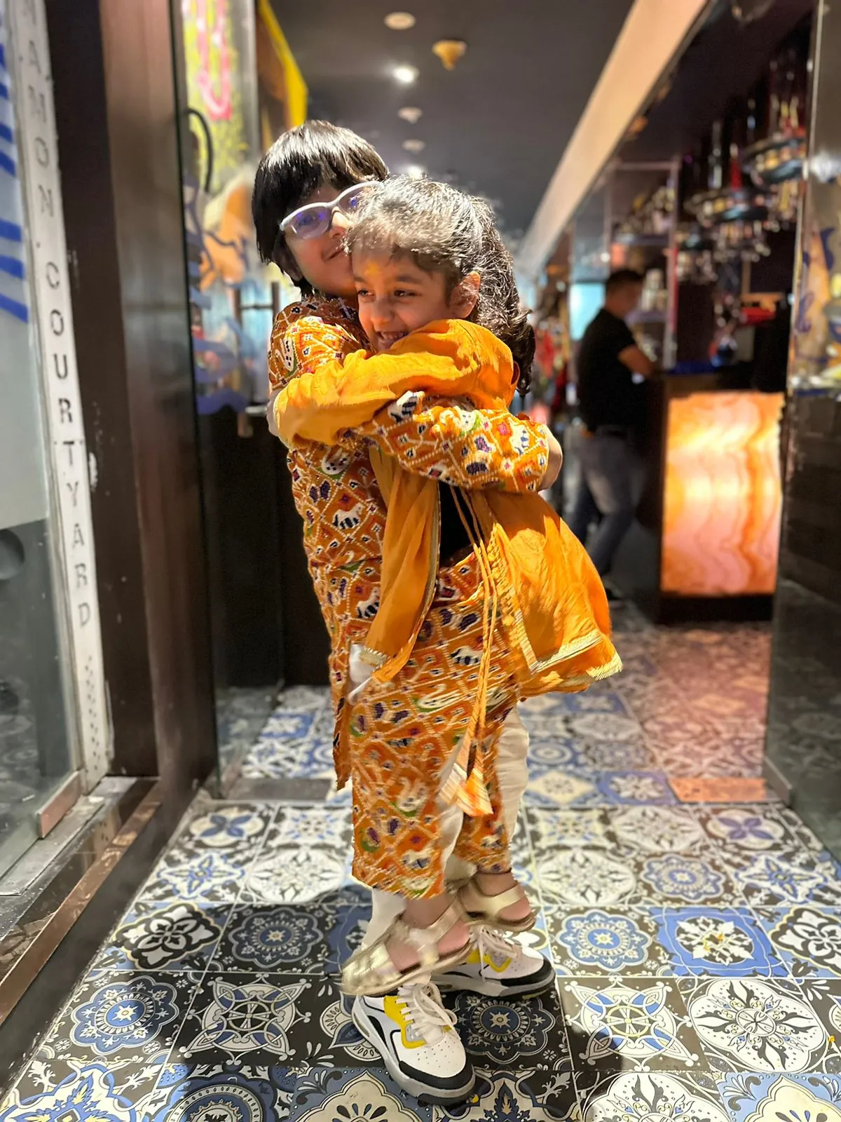 Two children in orange printed outfits hugging