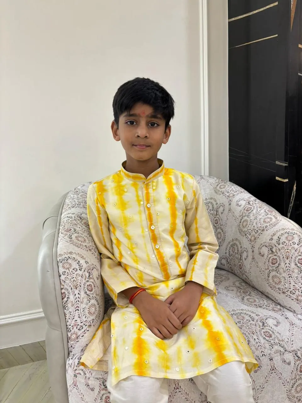 Boy in a yellow tie-dye kurta sitting in an armchair